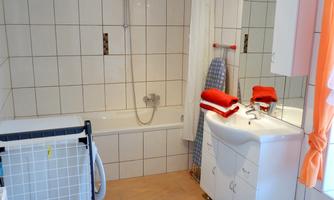A modern bathroom with a bathtub, shower, and a sink. There is a drying rack and towels in various colors.