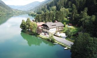 A picturesque lakeside with a cozy house surrounded by lush greenery. The mountains in the background and the calm water create a peaceful atmosphere.