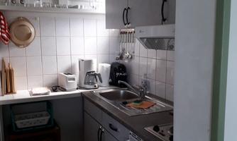 A small kitchen with modern appliances and bright walls. There is a table, several chairs, and a clock on the wall.