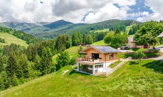 A beautiful wooden house on a green meadow in the mountains. In the background, forests and mountains are visible.