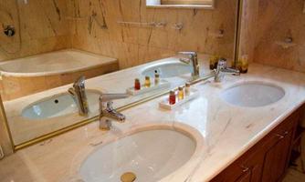 An elegant bathroom with a marble double sink and two basins. In the background, there is a bathtub and warm lighting.