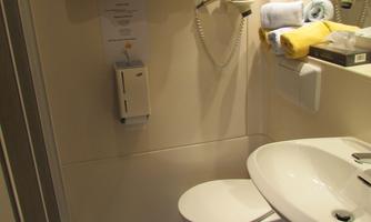 A small bathroom with a toilet, a sink, and a rug. Some yellow and blue towels are hanging on the wall.
