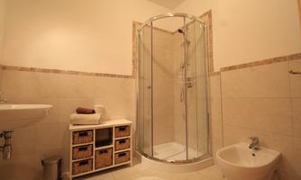A modern bathroom with a shower cabin, a sink, and a bidet. There is also a small shelf with baskets for storage.