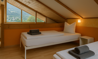 A cozy room with two single beds and large windows. The walls are painted in warm orange tones, creating an inviting atmosphere.