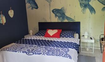A cozy bedroom with a large bed and blue bedding. Decorative elements and fish are depicted on the wall.