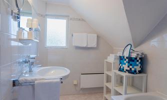 A modern bathroom with a sink, towels, and a window. There is also a white shelf with additional towels and a blue basket.