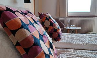 A bright bedroom with two beds and colorful cushions. The window offers a view of the outdoor area.