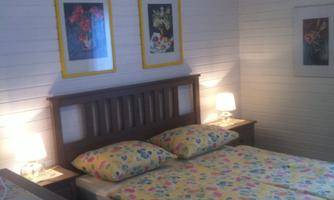 A cozy bedroom with a double bed and colorful bedding. Decorative pictures hang on the walls, and there are nightstands with lamps.