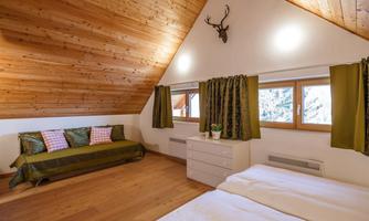 A cozy bedroom with a wooden ceiling and two single beds. There is a seating area with a green couch and large windows with green curtains.