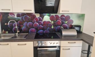 A modern kitchen with a granite countertop and a decorative backdrop of grapes. It includes a sink, a stove, and an oven.