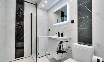 A modern bathroom with elegant, bright tiles and a large mirror. The shower is separated by a glass wall, and the fittings appear stylish and functional.