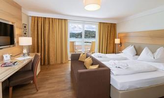 A modern hotel room with two beds and a cozy sofa. Large windows offer a beautiful view of the landscape.