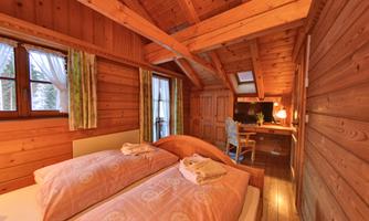 A cozy room with wooden paneling, two beds, and a desk. Generous windows provide plenty of daylight.