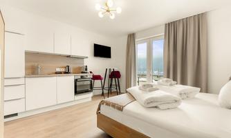 A modern room with a double bed, a kitchenette, and a dining table. Large windows provide plenty of natural light and a beautiful view.