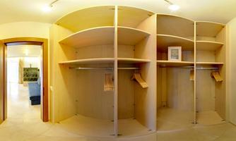 An empty wardrobe with open shelves and a bright interior. In the background, a room with a sofa can be seen.