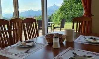 A cozy dining table with a view of the mountains and the green landscape. The large windows bring a lot of light into the room.