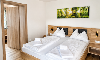 A modern bedroom with two beds and fresh white bedcovers. On the wall hangs a picture of a sunny forest.