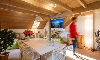 A modern furnished penthouse apartment with a large dining table and a television. Bright wooden walls and a cozy atmosphere characterize the space.