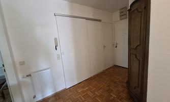 A bright hallway with a wooden floor and white walls.  
On the side stands an antique cupboard and there is a radiator on the wall.