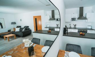 A modern apartment with an open living and dining area. The kitchen is elegantly designed and well-equipped, and there is a cozy living area with a black couch.
