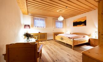 A cozy bedroom with a wooden ceiling and furniture. There is a large bed, nightstands, and a desk.