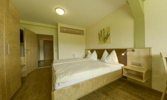 A modern bedroom with two beds and wooden-colored furniture. The walls are painted in soft colors, and there is a fresh plant picture.