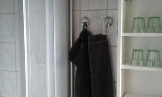 A bathroom with a shower cabin and a gray towel hanging on a hook. Next to the shower, there is a shelf with green glasses.