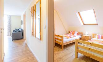 A bright hallway with a bedroom on the right side. The room is comfortably furnished with two beds and a window.