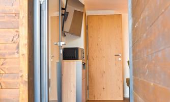 An inviting entrance to a modern room. You can see an open door, a television on the wall, and a wooden floor.