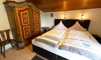 A cozy bedroom with a large, intricately decorated wardrobe and a double bed. The warm wood tones and traditional details create an inviting atmosphere.