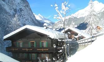 A picturesque chalet in the Alps, surrounded by snow-covered mountains. The clear blue sky enhances the wintry atmosphere.