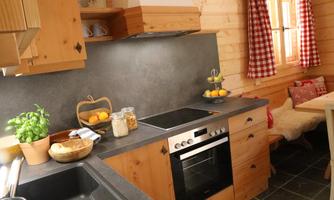 A cozy wooden-style kitchen with modern appliances. The windows have red checked curtains and fresh ingredients are provided.