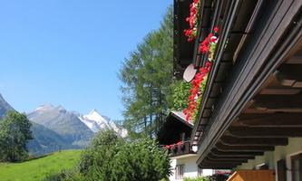 A picturesque house with flower boxes and a beautiful view of the mountains. Green meadows and a blue sky complete the idyll.