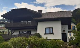 A charming house with a sloped roof and a large balcony.  
Surrounded by green bushes and a beautiful landscape.