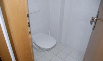 A simple bathroom with a toilet and white walls. The floor is tiled and the door is made of wood.