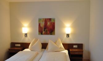 A bright room with two beds and a colorful painting on the wall. The wall lamps provide a pleasant lighting.