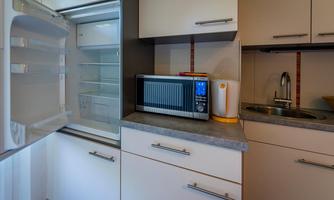 A modern kitchen with an open refrigerator, a microwave, and a kettle. The cabinets are designed in neutral colors and provide a practical workspace.