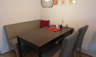 A cozy dining area with a wooden chair and a bench. The table is decorated with a red placemat and a small flower.