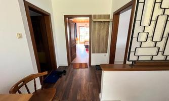A bright corridor with wooden flooring and several doors. On the left side, there is a table with a chair.