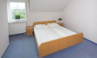 A simple bedroom with a double bed and two nightstands. The room has a window overlooking nature.