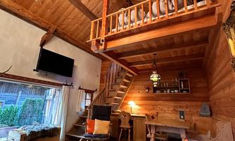 A cozy wooden room with a raised sleeping area and a large chandelier. The space is warmly designed and has an inviting atmosphere.