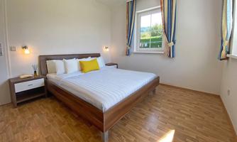 A modern bedroom with a large bed and bright walls. There are windows with colorful curtains and a nightstand next to the bed.