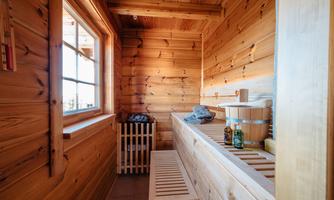 A cozy sauna with wooden paneled walls and windows that let in plenty of light. On the bench, there are sauna accessories and refreshing drinks.