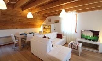 A cozy living room with white furniture and a wooden ceiling. There is a dining area, a television, and plenty of daylight.