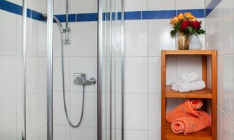 A bright bathroom with a shower cabin and white tiles. A shelf with towels and a bouquet of flowers completes the scene.