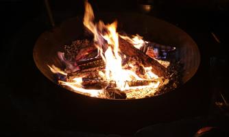 A warm campfire in a fire bowl. Flames flicker over wooden logs and create a cozy atmosphere.