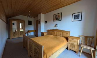 A cozy bedroom with a wooden ceiling and country-style furniture. The room is bright and inviting, featuring a large bed and a beautiful mirror.