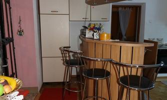 A cozy kitchen with a wooden bar and high chairs. The floor is covered with a red carpet, and the walls are painted in soft colors.