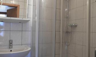 A bathroom with a modern shower and a sink. The walls are tiled with white tiles.