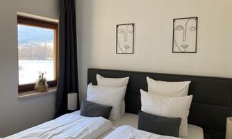 A cozy bedroom with two beds and many pillows. Two abstract pictures hang on the wall, and a window lets in daylight.